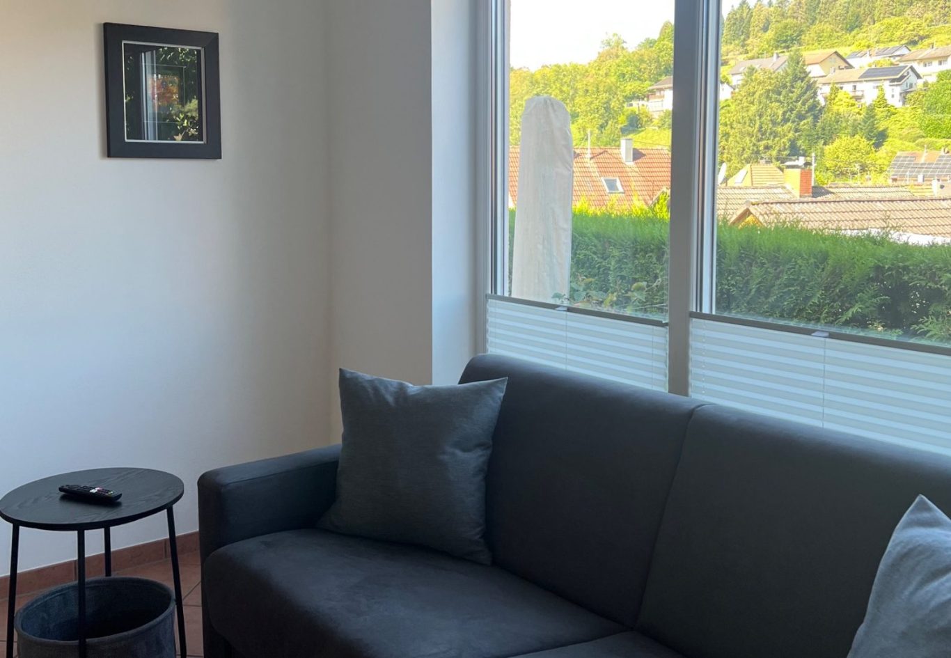 Apartment 1, Wohnzimmer Schwarzes Sofa mit Buch und Tasse auf einem Tisch. Warmes, minimalistisches Ambiente.